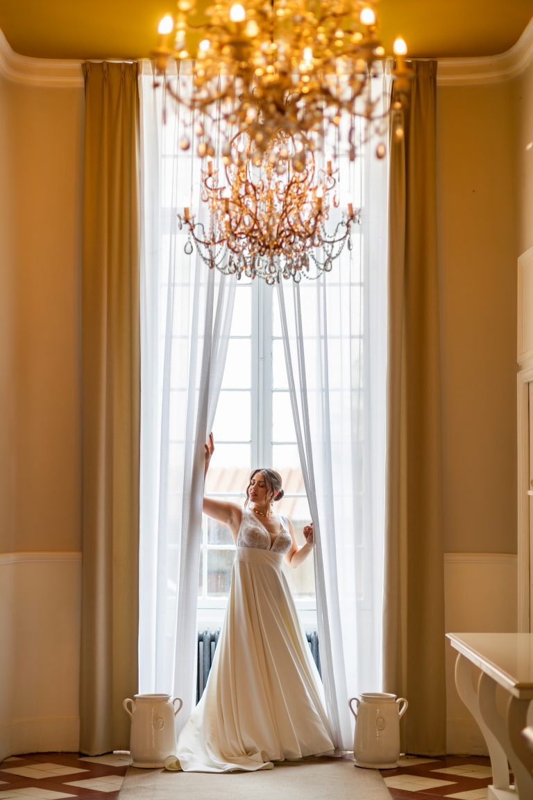 Mariée élégante posant sous un lustre doré dans un hôtel de luxe en Provence – lumière naturelle en Côte d’Azur