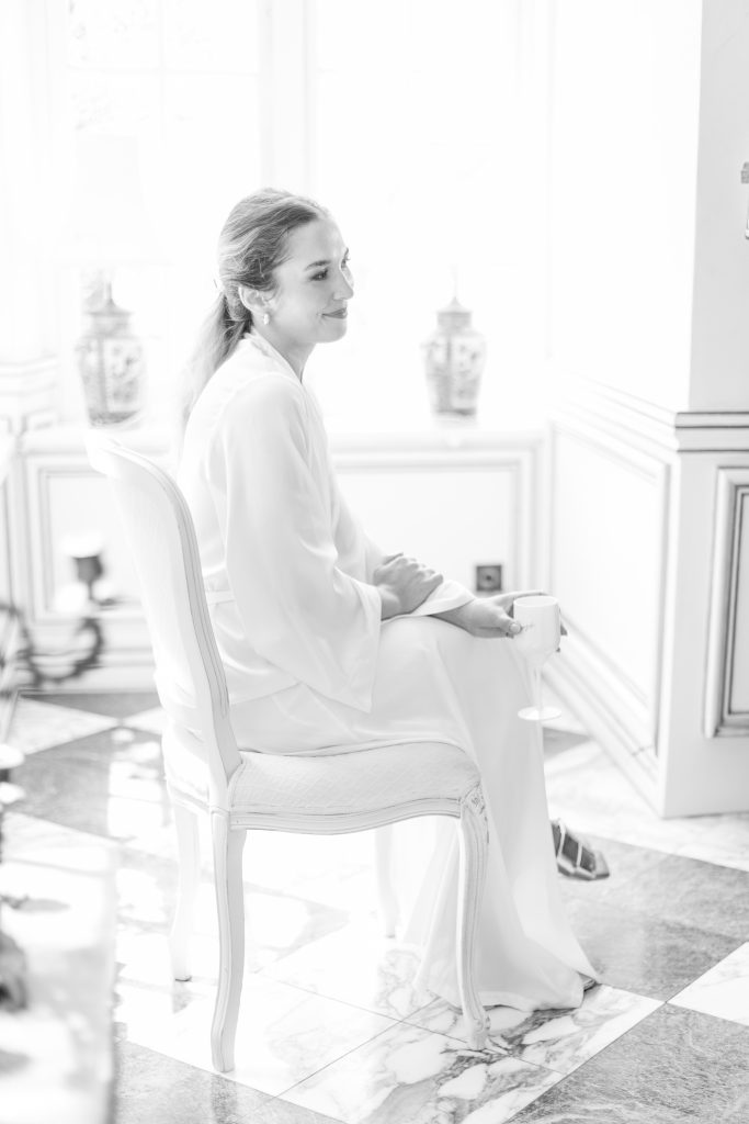 Portrait doux et lumineux d’une mariée dans sa robe de préparation, assise près d’une fenêtre au Château de Robernier.