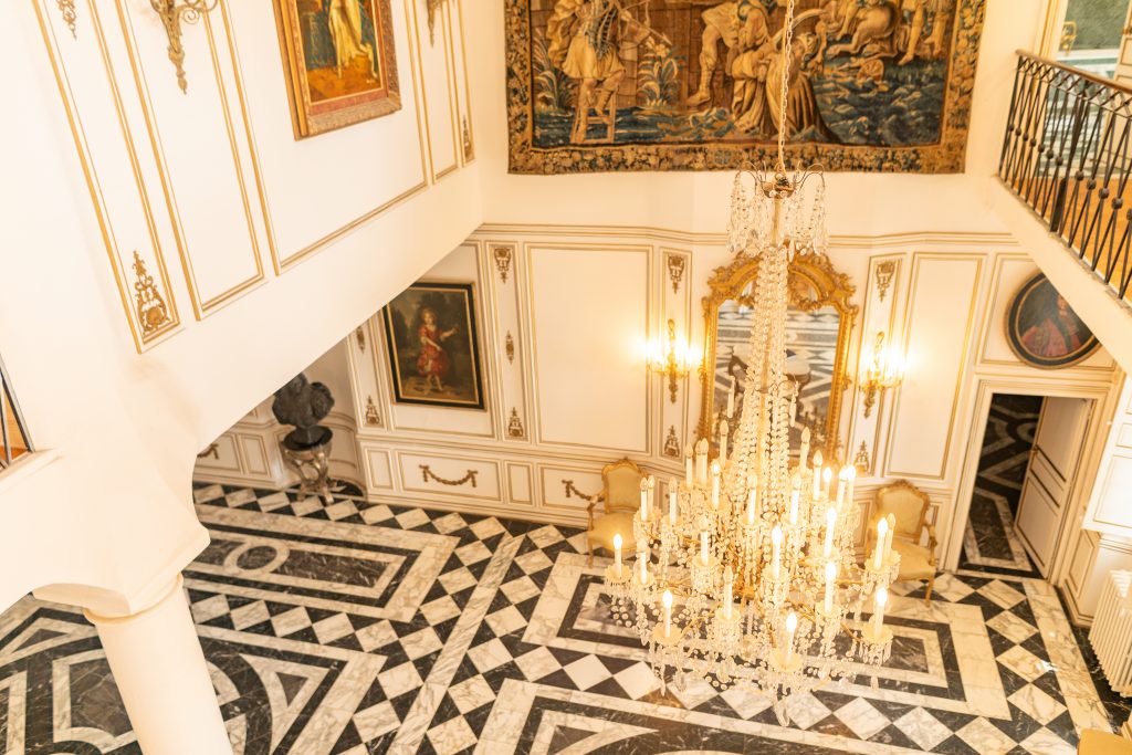 Vue plongeante sur le hall du Château de Robernier avec lustre en cristal, tapisseries et sols en marbre.