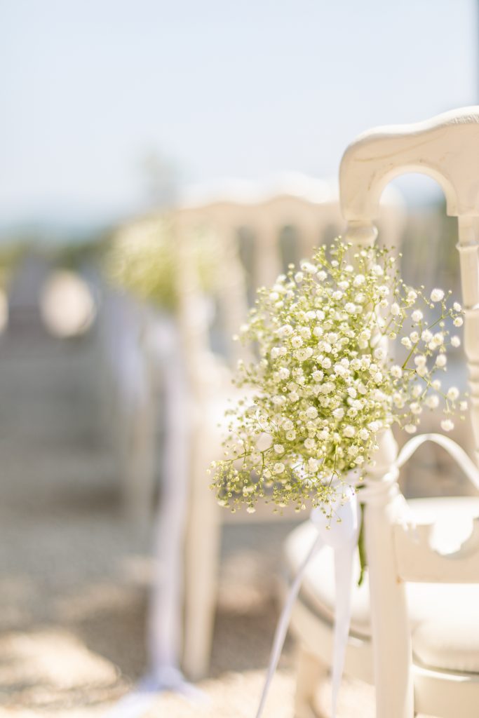 Détail d’un bouquet de gypsophile attaché à une chaise blanche pour la cérémonie extérieure au Château de Robernier.