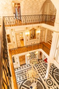 Vue intérieure du hall monumental du Château de Robernier avec lustre en cristal, moulures dorées et sol en marbre graphique.