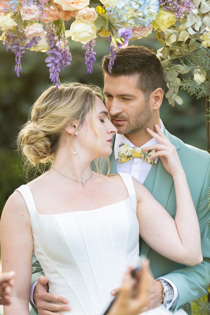 Couple de mariés élégants sous une arche florale romantique, lors d’un mariage raffiné en Provence inspiré de l’esthétique Bridgerton.
