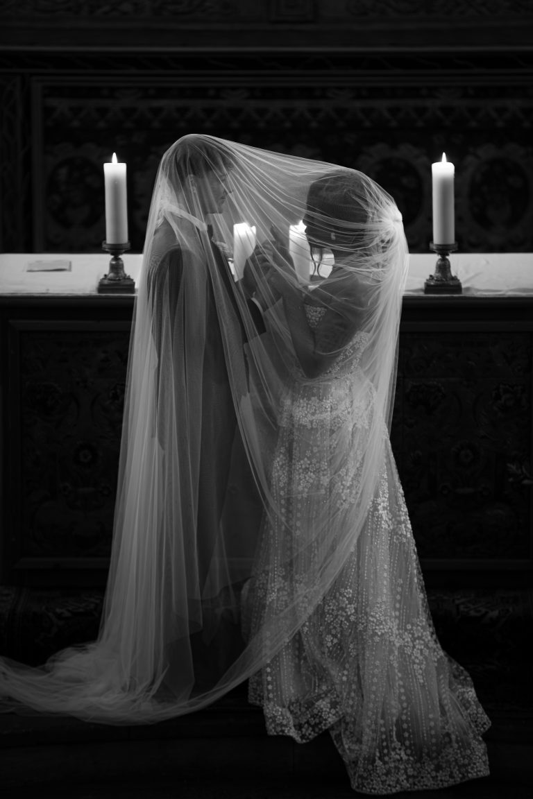 Couple de mariés sous un voile de tulle devant l’autel, éclairé à la bougie, photographié en noir et blanc par Studio JOLY Photographie lors d’un mariage de luxe en Provence.