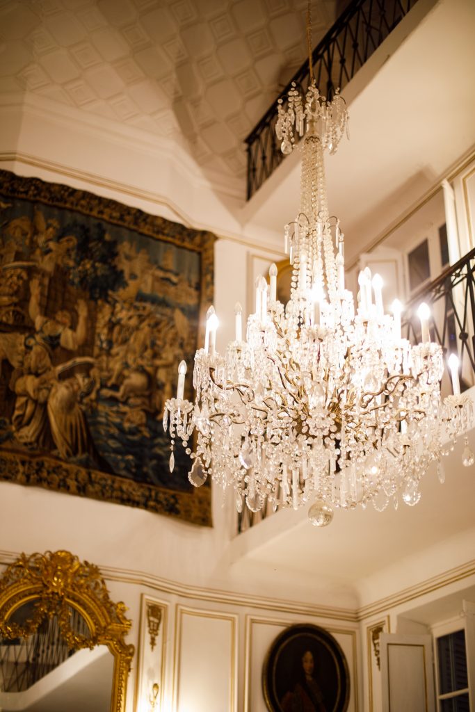 Lustre monumental en cristal suspendu dans le hall du Château de Robernier, avec tapisserie et miroir doré.